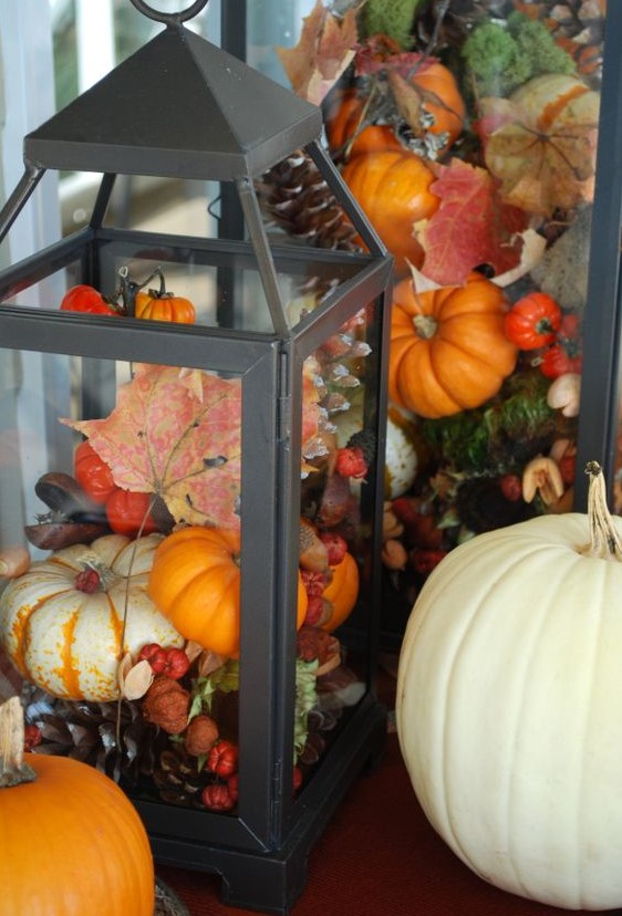 a black lantern filled with pinecones and fake pumpkins, berries and leaves for a bright fall display