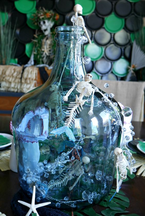 a seaside decoration of a large bottle with mermaid skulls, bebbles, greenery and starfish is amazing for Halloween
