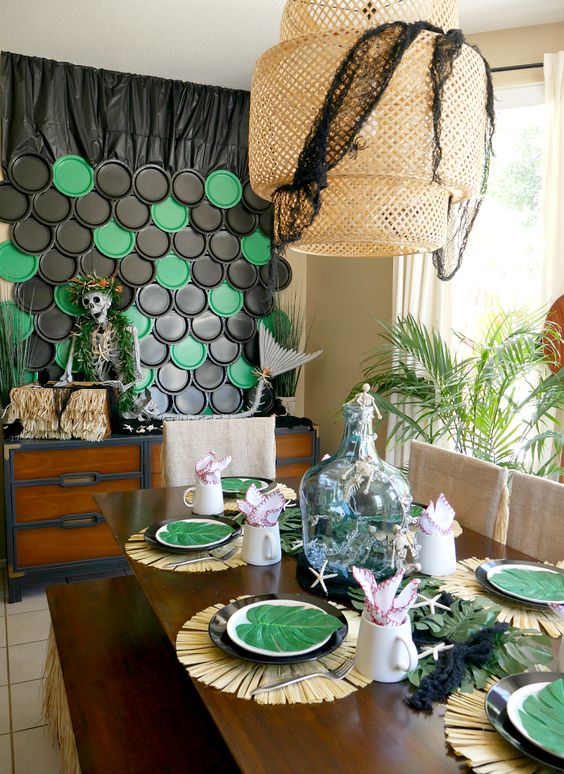 a tropical Halloween tablescape with a placemat, plates and tropical leaves, starfish and black cheesecloth on the lamp