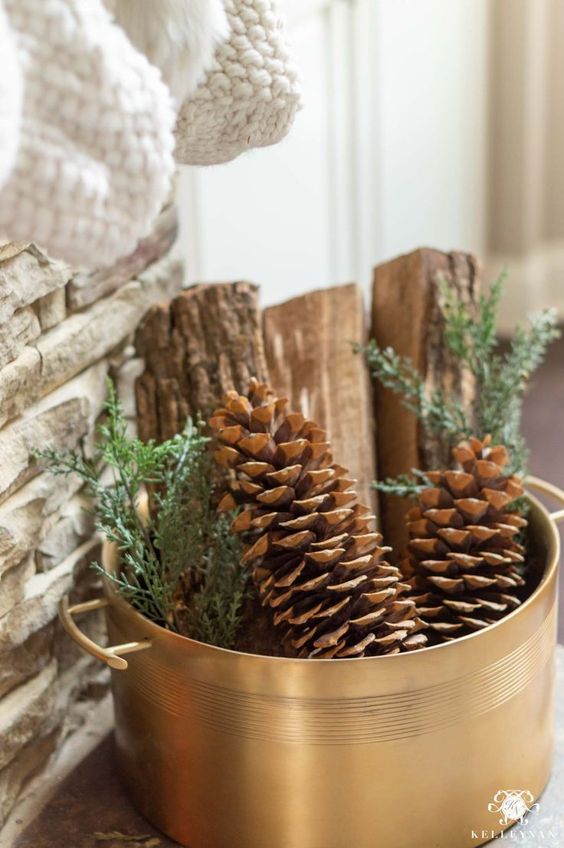 a copper pan with pinecones, firewood and greenery is a cool natural decoration for both fall and winter