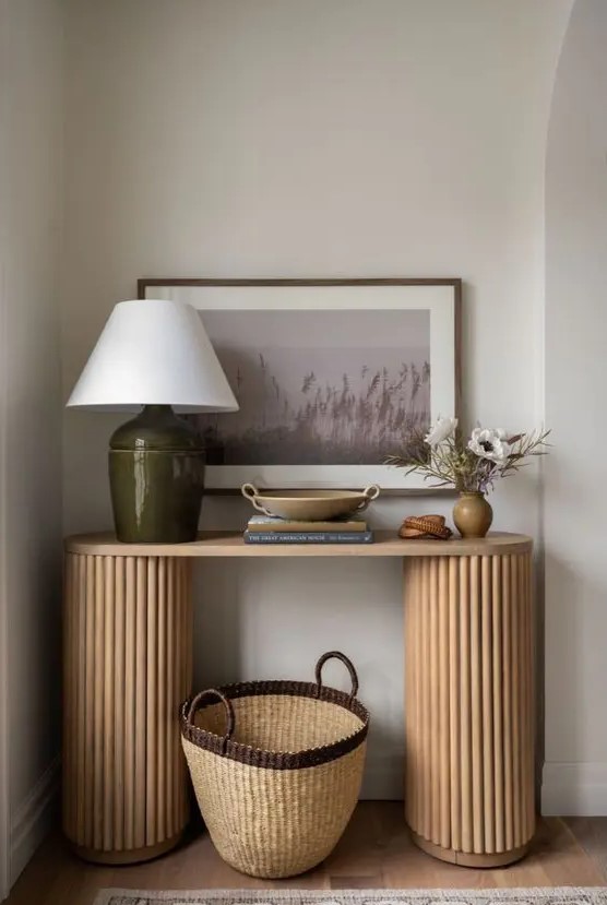 a beautiful entryway console table with fluted legs, a table lamp, some decor, an artwork and a basket for storage is all cool