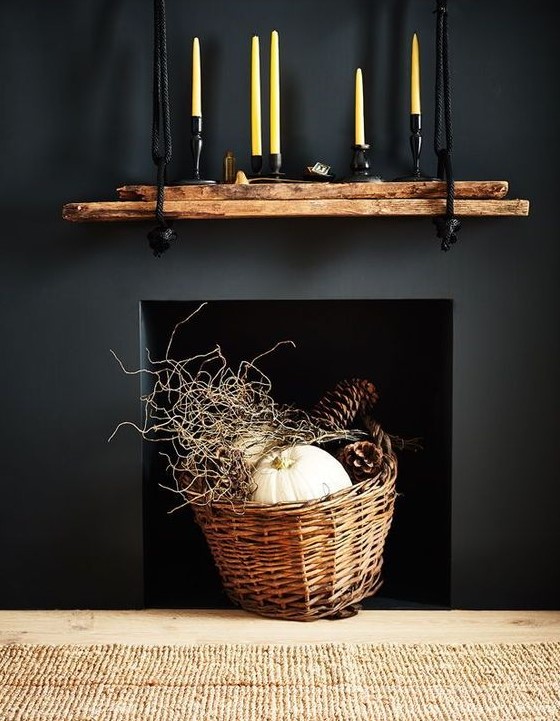 a modern rustic and woodland decoration   a black built in fireplace with a basket with twigs, pumpkins and large pinecones is awesome for fall