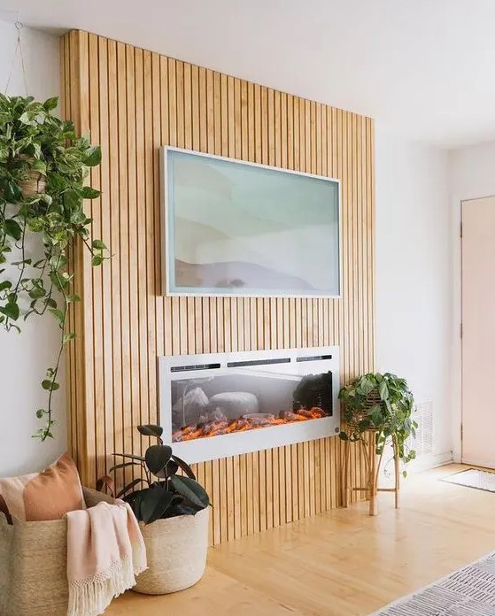 an electric fireplace with a fluted surround that includes an artwork, potted greenery and baskets for a cozy feel