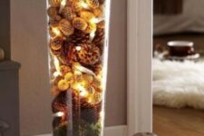 50 a tall glass vase filled with moss, various pinecones, dried blooms and lights is a natural fall decoration