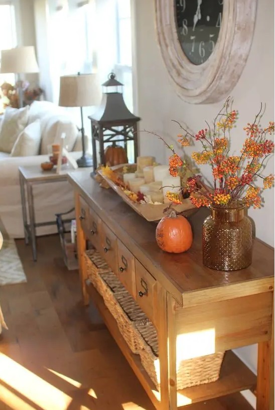 a console table with a fall leaf arrangement, a pumpkin and a wooden bowl with leaves and candles for the fall
