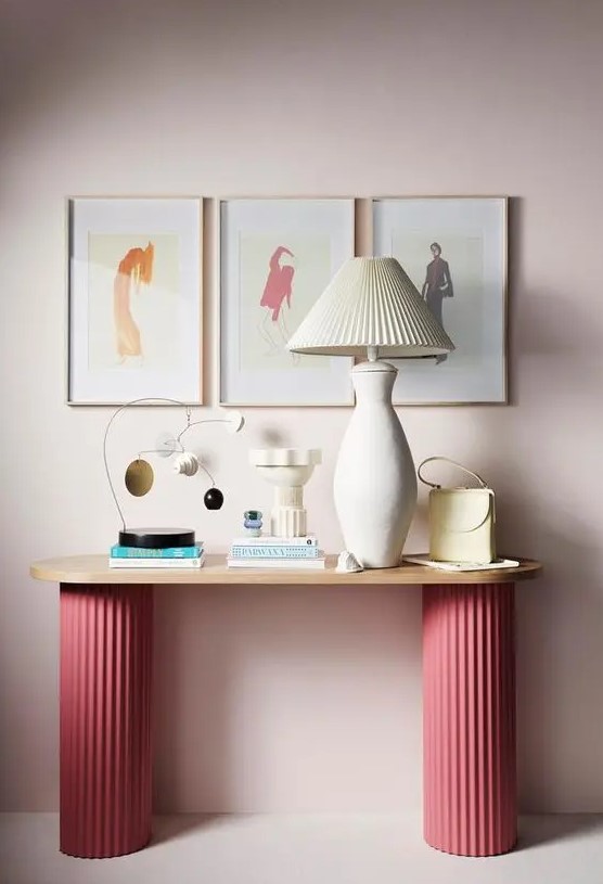 An eye catching console table with pink fluted legs, a lamp with a fluted lampshade, some deco and a gallery wall