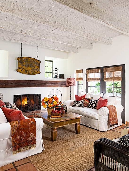 a traditional fall living room with a fireplace and a metal screen, white sofas, printed pillows, a vintage sign, bold flower and leaf arrangements to celebrate the fall