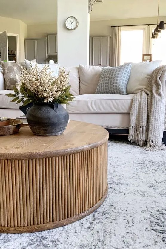a neutral living room with a creamy sofa and pillows, a round fluted coffee table, a printed rug and some lovely decor