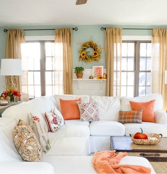 bright orange textiles, bright fall blooms and a sunflower wreath bring a fall feel to the neutral living room