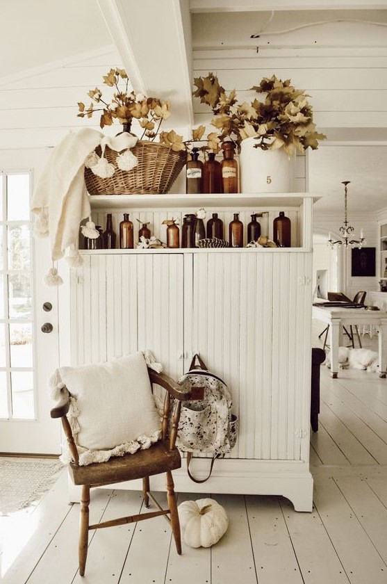 fall leaves arranged in vintage apothecary bottles and a white pumpkin add a fall feel to the space