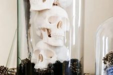 a Halloween cloche with black seed pods and stacked skulls is a cool idea for a Halloween party