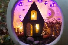 a Halloween diorama in a white pumpkin, with hay, pebbles, a black house, some bat-shaped lights and a moon