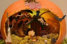 a Halloween pumpkin diorama with moss, pumpkins, pinecones, a broom, bats and a small house with lights behind it is a great idea