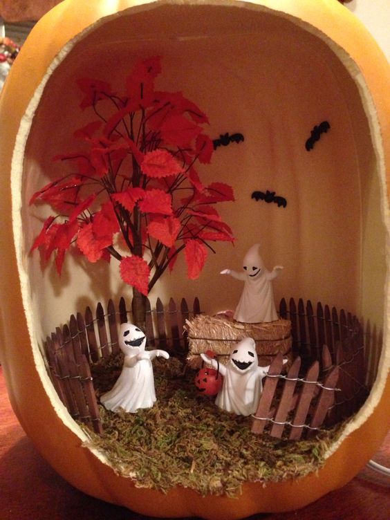 a Halloween pumpkin terrarium with hay, a fence, some ghosts, a tree with bold leaves and black bats is cool
