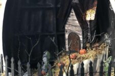 a Halloween pumpkin terrarium with hay, pumpkins, a fence, a haunted house and some branches