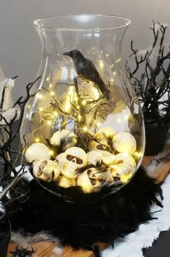 a Halloween terrarium of a large jar, skulls and lights, branches and spiderweb, a blackbird is a stylish idea for moody decor