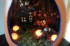 a Halloween terrarium with greenery, lights, a witch and a haunted house with a berry tree is a cool idea