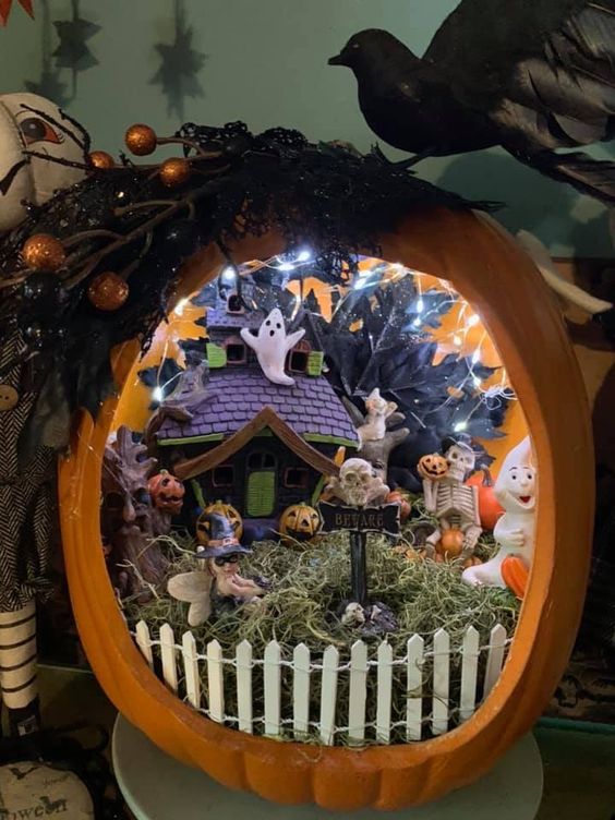a Halloween terrarium with hay, a fence, some ghosts, pumpkins, a haunted house and lights plus black leaves