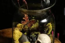 a Halloween terrarium with moss, pebbles, butterflies, dried blooms and a small skull is a bold and cool idea for Halloween decor