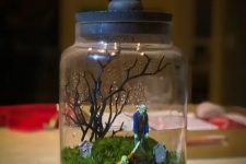 a Halloween terrarium with pebbles, moss, zombies, a tree and some tombstones is a cool and catchy idea