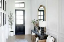 a black and white entryway with a black door, a black console table, a neutral chair, a black and gold lantern and a gallery wall