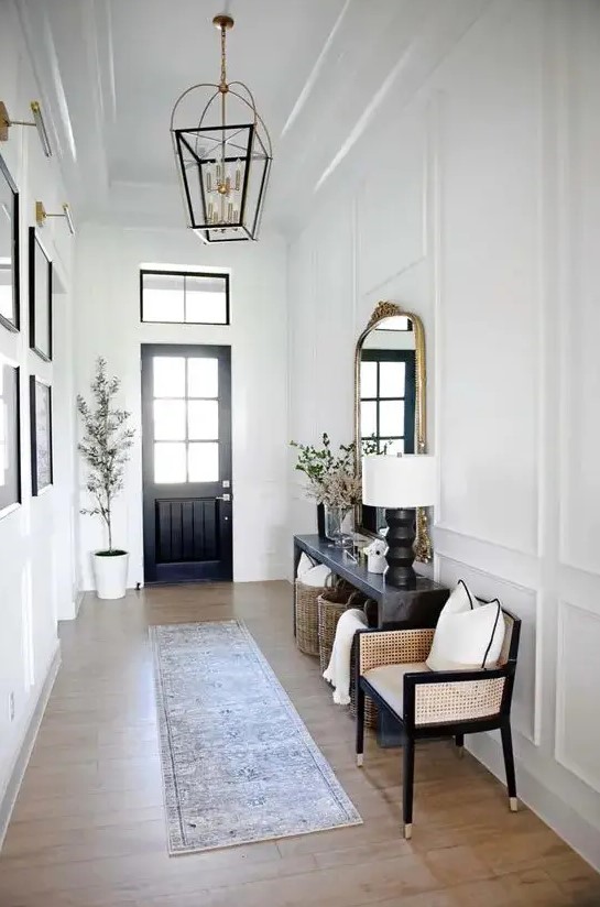 a black and white entryway with a black door, a black console table, a neutral chair, a black and gold lantern and a gallery wall