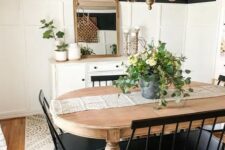a black and white farmhouse dining room with a white sideboard, a stained vintage table, black chairs and a bench and a vintage chandelier