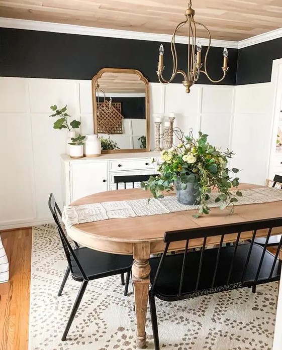 a black and white farmhouse dining room with a white sideboard, a stained vintage table, black chairs and a bench and a vintage chandelier