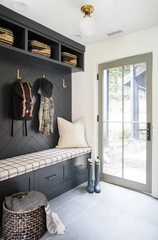 a black and white farmhouse mudroom with a black accent wall and built in storage units, a basket for storage and a glass door