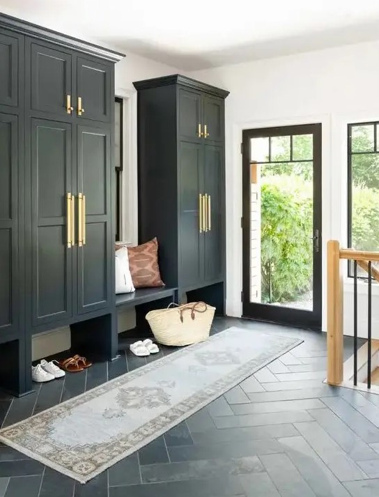 a black and white mudroom in farmhouse style, with large wardrobes, a built in bench, a printed rug and a glass door