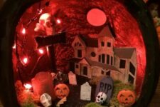 a black pumpkin diorama with red lights and a paper house, a moss graveyard and pumpkins plus a red moon