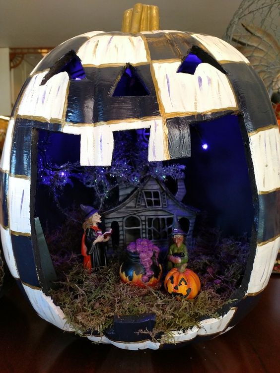 a checked pumpkin as a Halloween terrarium, with hay, a haunted house, witches, a caulron and some pumpkins