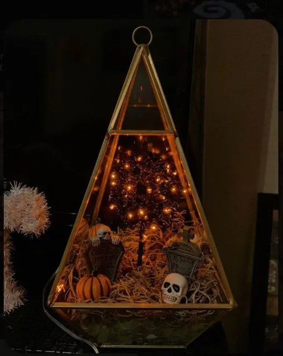 a chic Halloween terrarium with moss, tombstones and skulls, jack-o-lanterns and a lit up tree is a cool idea