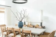 a chic modern farmhouse dining space with a large table, wooden and woven chairs, a metal chandelier and a console and lamps