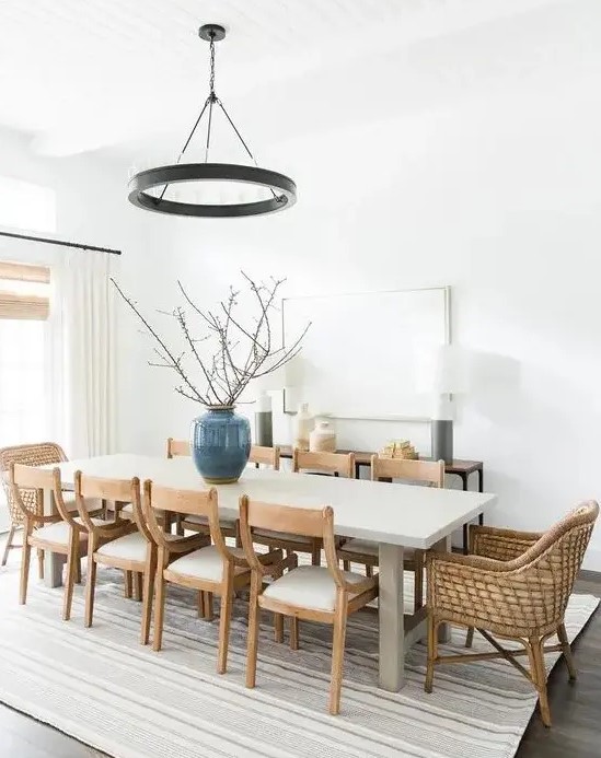 a chic modern farmhouse dining space with a large table, wooden and woven chairs, a metal chandelier and a console and lamps