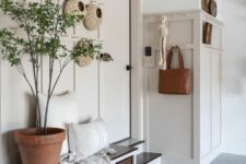 a chic modern farmhouse entryway with greige paneling, a built-in bench with cubbies, a potted plant and some decor