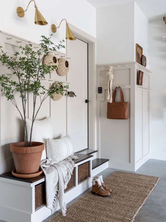a chic modern farmhouse entryway with greige paneling, a built in bench with cubbies, a potted plant and some decor