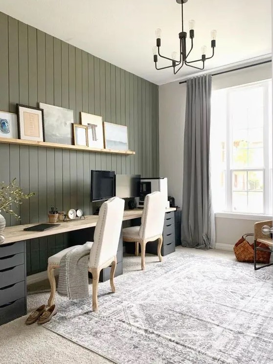 a chic modern farmhouse home office with a grene shiplap wall, a large double desk, neutral chairs and a black chandelier