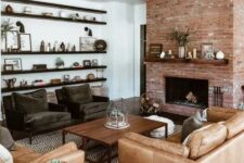 a chic modern farmhouse living room with a red brick fireplace, dark chairs, a tan leather sofa and chair, a coffee table and dark-stained shelves