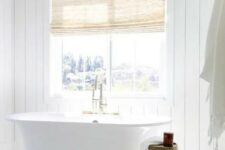 a chic white bathroom with shiplap walls, a mosaic tile floor, a tub by the window and a fabric covered vanity