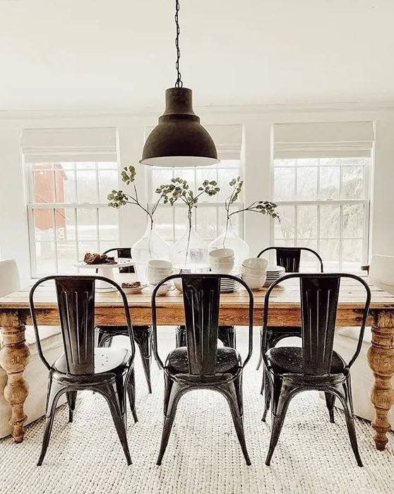 a classy modern farmhouse dining room with a stained table, black metal chairs and a pendant lamp and some greenery