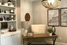 a clean and simple modern country home office with grey walls, a white storage unit, a trestle desk, a leather chair and a wooden bead chandelier