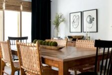 a contrasting modern farmhouse dining room with a stained table, woven leather and black wooden chairs, a mini gallery wall and curtains