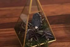 a cool mini Halloween terrarium with moss, faux greenery and leaves, skulls, a tombstone and pebbles