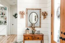 a cool modern farmhouse entryway featuring a stained console table, a mirror in a rustic frame, burlap bows and some floral arrangements