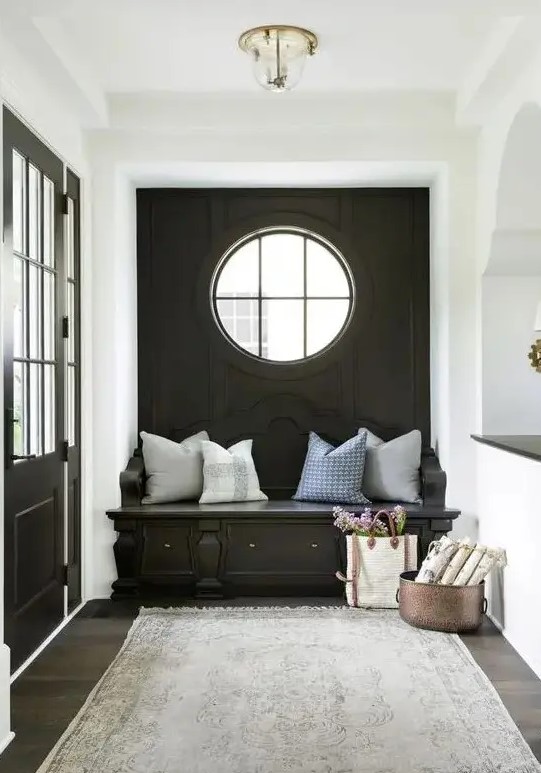 a cozy black and white mudroom with a black accent wall, a porthole window and a built-in bench, neutral pillows and a grey rug