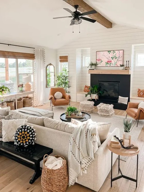 a cozy modern farmhouse living room with a fireplace, a creamy sofa, amber chairs, a console table with baskets and some greenery