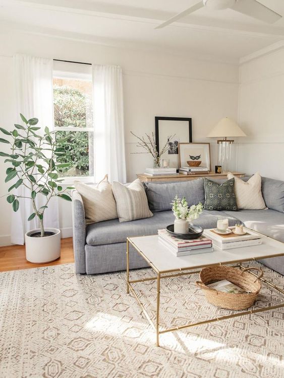 a cozy neutral modern famrhouse living room with a stained dresser, a grey sofa with many pillows, a coffee table and greenery