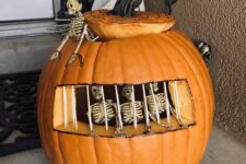 a creative carved pumpkin showing off a jail for skeletons, with some of them inside and some outside for Halloween decor