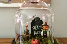 a cute and lovely Halloween cloche with moss, a black cat, a tombstone, pumpkins and lights on top